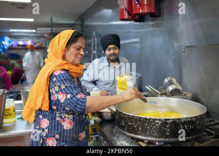 A woman volunteer in a Sikh langar communal kitchen cooks a vegetarian dish to feed worshippers, visitors and strangers. At a temple in Queens, NYC. Stock Photo