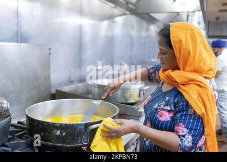 A woman volunteer in a Sikh langar communal kitchen cooks a vegetarian dish to feed worshippers, visitors and strangers. At a temple in Queens, NYC. Stock Photo