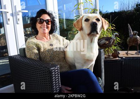 Attractive mature female sitting on a patio with her pet yellow labrador retriever - John Gollop Stock Photo