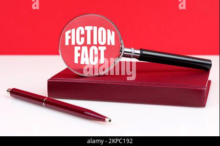 Business and finance concept. On a white and red background, a notebook, a pen and a magnifying glass, inside which the inscription - Fiction Fact Stock Photo