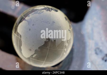 Environmental concept. Glass ball - a planet lying on the grate of a drainage pit to collect water. Contaminated water flows down the drain. Stock Photo