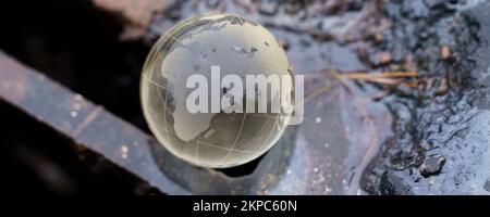 Environmental concept. Glass ball - a planet lying on the grate of a drainage pit to collect water. Contaminated water flows down the drain. Stock Photo
