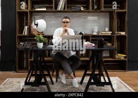 stylish adult european woman with short haircut sitting in strong office looking at camera Stock Photo