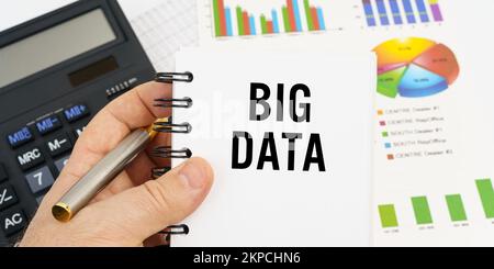 Finance and economics concept. The man is holding a pen and a notebook with the inscription - BIG DATA. In the background are financial charts, charts Stock Photo