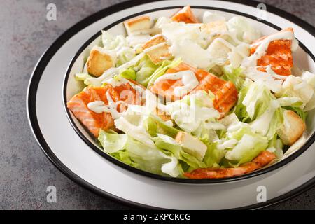 Plate with fresh caesar salad with Grilled Salmon, Croutons, Parmesan, Caesar Dressing closeup on the plate on the table. Horizontal Stock Photo