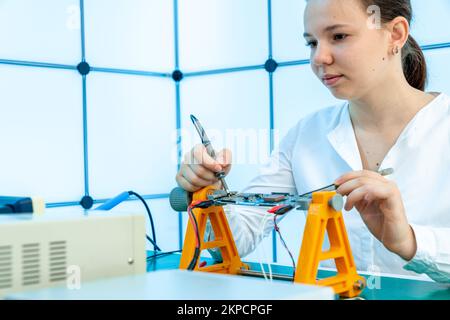 repairing a printed circuit board in an electronics laboratory a young woman measures voltage at test points Stock Photo