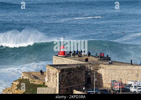 People watching the big giant waves crashing near the Fort of Nazare Lighthouse in Nazare, Portugal. Biggest waves in the world. Stock Photo