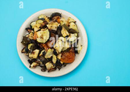 Mixed baked vegetables on light brown dish on blue Stock Photo