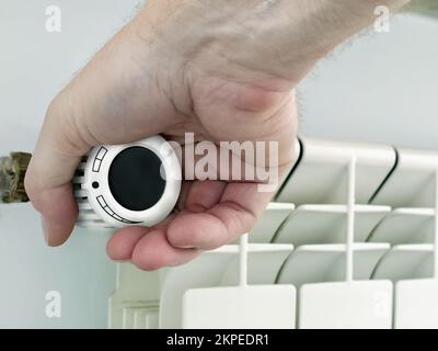 Closeup of male hand reducing central heating radiator temperature in the room using thermostat Stock Photo