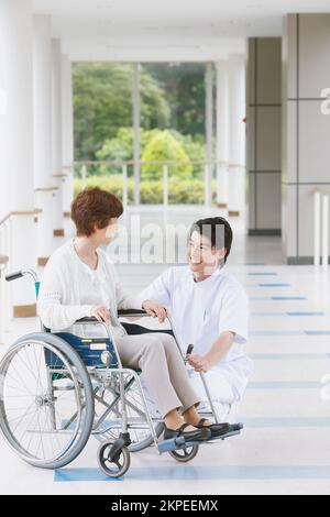 Japanese senior woman in a wheelchair and a young male nurse conversing in the hallway Stock Photo