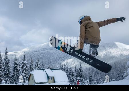 Marmaros, The Carpathians, UKRAINE - Feb 16 2021: An active freerider on a snowboard jumping above the house Stock Photo