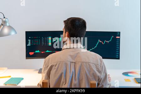 Rear view of young caucasian man finance broker analyzing stock graphs while trading from home Stock Photo