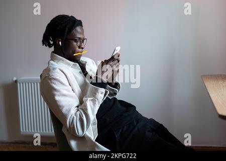 Young focused African guy student holding mobile phone, surfing educational information online Stock Photo