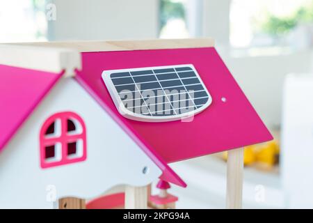 A solar cell is installed on the pink roof of a model wooden toy house. Stock Photo