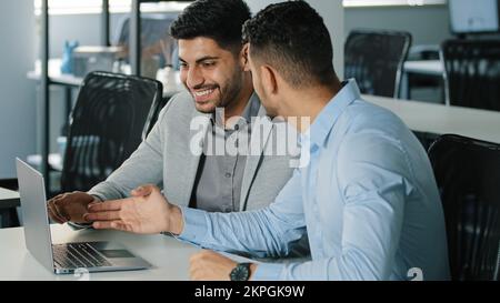 Two successful Arab male businessmen satisfied with result of negotiations, concluded contract. Smiling young colleagues Indian employees sitting in Stock Photo