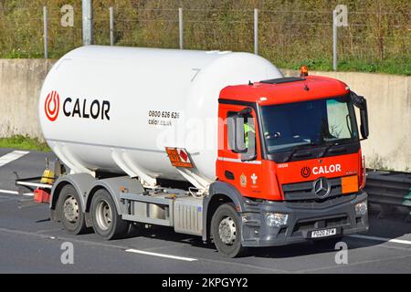 Red lorry truck with driver in cab of Mercedes chassis cab white Calor delivery gas tanker showing Hazchem chemical warning plates on UK motorway road Stock Photo