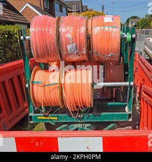 Residential street pavement closed off by multiple fibre optic cable drums on trailer feeding broadband into trenches & junction boxes England UK Stock Photo