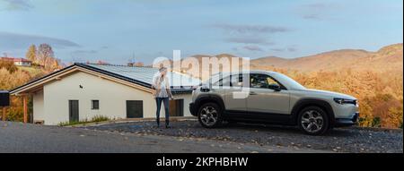 Young woman charging her electric car in home, sustainable and economic transportation concept. Stock Photo