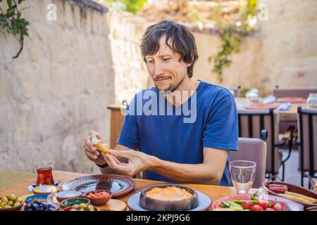 Man eating turkish breakfast. Turkish breakfast table. Pastries, vegetables, greens, olives, cheeses, fried eggs, spices, jams, honey, tea in copper Stock Photo