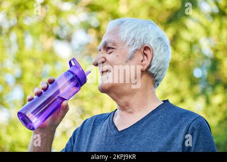 Mature man holds plastic reusable bottle drinking still mineral water during morning work out or stroll in summer park, caring about health, relieving Stock Photo
