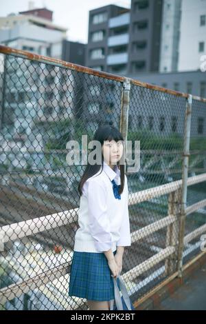 Japanese female high school student leaning against the fence Stock Photo