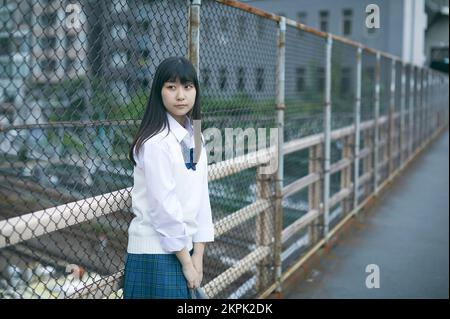 Japanese female high school student leaning against the fence Stock Photo