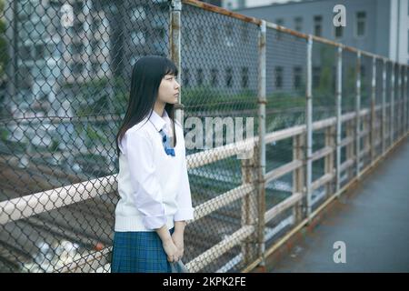 Japanese female high school student leaning against the fence Stock Photo