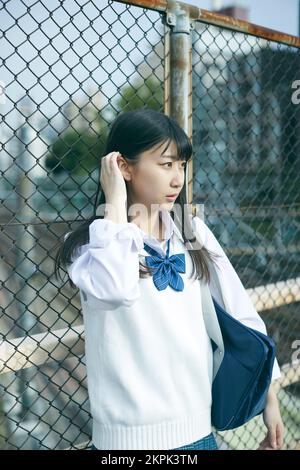 Japanese female high school student leaning against the fence Stock Photo