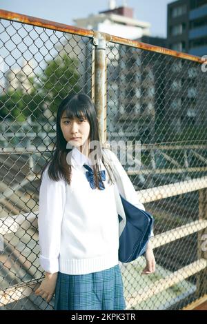 Japanese female high school student leaning against the fence Stock Photo