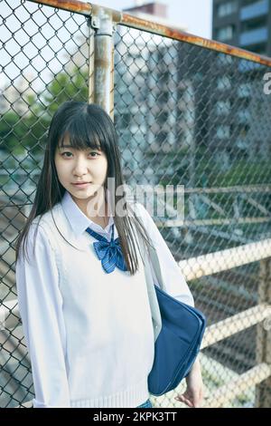 Japanese female high school student leaning against the fence Stock Photo