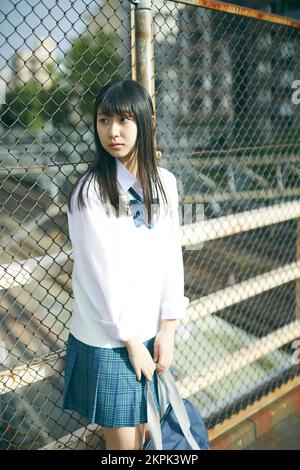 Japanese female high school student leaning against the fence Stock Photo