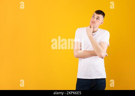 Pensive caucasian man looking aside at copy space and touching chin, thinking about interesting offer, yellow background Stock Photo
