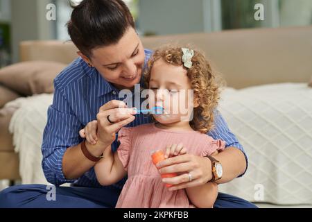 Joyful girl blowing soap bubbles for the first time, mother explaining how to do it right Stock Photo