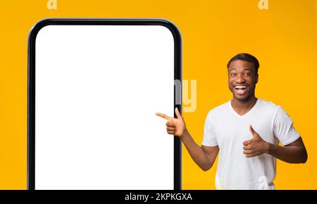 Great Offer. Joyful Black Man Pointing On Huge Smartphone With Blank Screen Stock Photo
