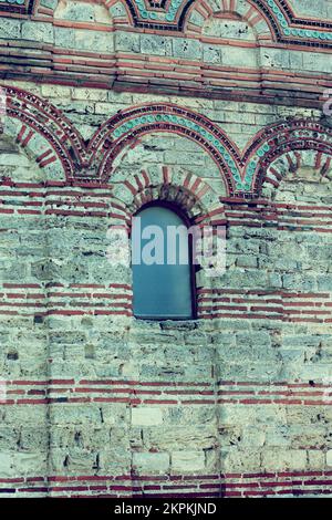 Facade of an old high wall with a window in fortress. Wall is made of brick and multi-colored mosaics, interesting views for tourists Stock Photo