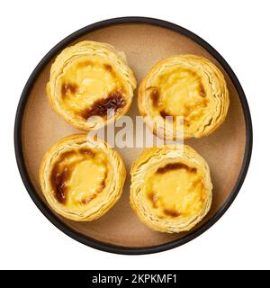 Four portuguese custard egg tarts on a beige rustic ceramic plate isolated on white. Top view. Stock Photo