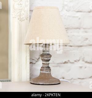 Stylish retro beige lamp with a decorative wooden knife stands on bedside table in bedroom. Stock Photo
