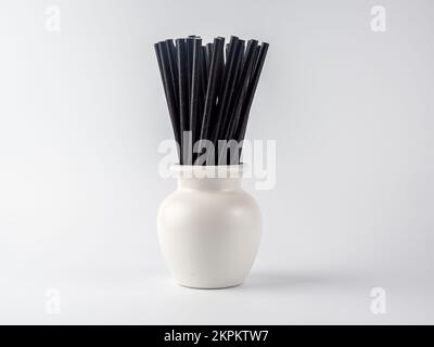 white vase pot containing black bio degradeable bamboo cocktail straws on a white background Stock Photo