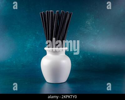 white vase pot containing black bio degradeable bamboo cocktail straws on a green background Stock Photo