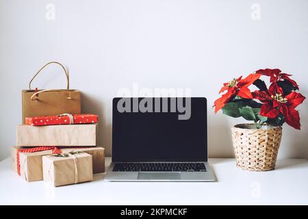 Blank display screen laptop computer with Poinsettias Christmas Flower and gift boxes on white table. Home office desk workspace with Mock up copy Stock Photo