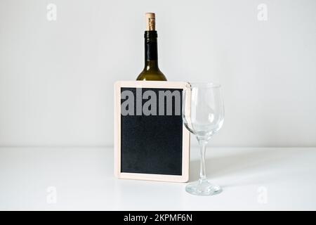 Bottle of wine, glass and empty sign mockup. Bottle of wine with empty glass and blackboard mockup on table. Stock Photo