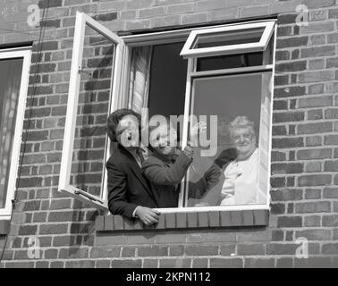 1980s, historical, standing at a window of their new home with a housing executive a couple with their daughter pose for a publicity photo, with the man holding the keys, England, UK. Stock Photo
