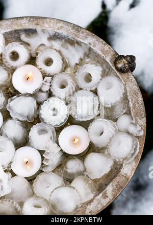 Handmade garden ice decoration in shape of mini bundt, Christmas trees, snowman with burning tea lights candles on rustic metal plate. Stock Photo