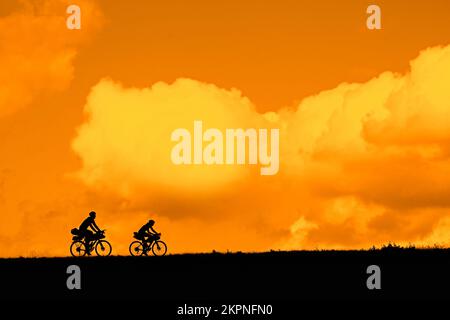 Couple of young cyclists riding their touring bicycles silhouetted against orange sunset sky in summer Stock Photo