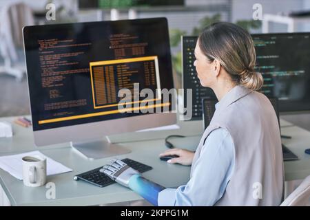 Female programmer with prosthetic arm working on computer in office of IT company Stock Photo
