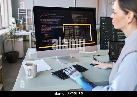 Software developer with prosthetic arm checking programming code on computer screen Stock Photo