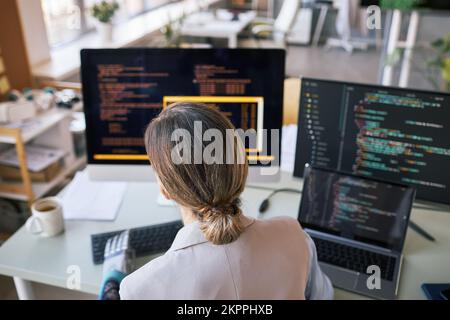 Female developer checking programming code on computer, view from back Stock Photo
