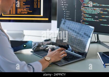 Closeup image of software developer with bionic arm working on laptop, creating new application Stock Photo