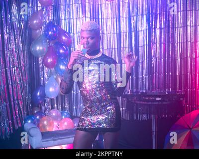 Non-binary person drinking happily at a party Stock Photo