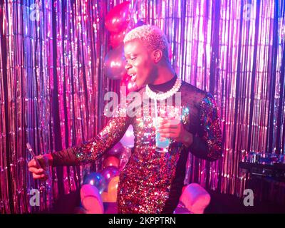 Non-binary person drinking happily at a party Stock Photo